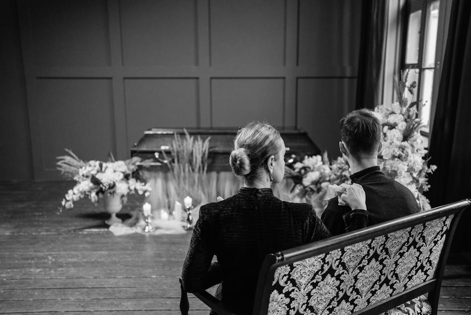 A black-and-white photograph of two individuals seated on a patterned wooden bench inside a room with wooden paneling. They are facing away from the camera, with the woman on the left and the man on t
